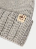 Close-up of a gray knit beanie with a brand tag featuring a logo on a white background #color_high-rise