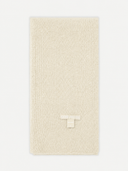 A cream-colored ribbed knit scarf with a small woven logo patch near the bottom, displayed flat against a light gray background.