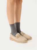 Person wearing gray socks and beige loafers on a white background.
