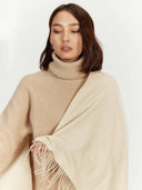 Woman wearing a beige sweater and holding a beige scarf against a white background