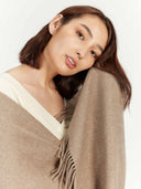 close up side view of a woman wearing a beige scarf with fringe on a plain background