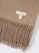 Beige scarf with fringe and a brand tag on a white background