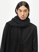 close up front view of a man wearing a black scarf over a matched color coat.