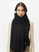 A person wearing a black oversized woven scarf that could also serve as a blanket.