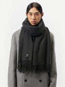 close up front view of a man wearing an oversized cashmere woven scarf in dark gray color over a gray coat in a light gray background.