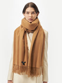 Woman wearing a brown scarf with a visible brand logo on a white background  #color_almond