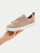 Beige sneaker with white sole held by a hand on a light gray background #color_taupe