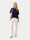 Woman wearing a navy top and white pants with a white bag on a light gray background #color_navy