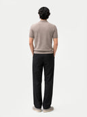 back view of a man wearing a beige shirt and black pants on a white background