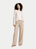 Woman wearing a white sweater and beige pants on a white background #color_whisper-white