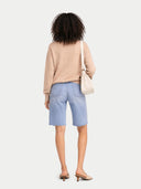 back view of a woman wearing a beige sweater and light blue shorts with a white background #color_beige
