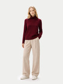 Front view of a woman wearing a burgundy sweater and beige pants on a white background #color_zinfandel