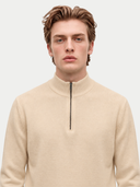 A man wearing a light beige quarter-zip mock neck sweater, shown from the chest up against a solid light gray background.