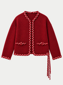 A red cropped cardigan jacket with braided trim details, featuring two front pockets with decorative braided buttons and a braided tie detail at the hem, shown on a plain white background.