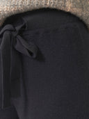 Close-up of a black garment with a tie detail against a textured brown background #color_black