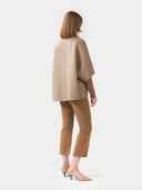 back view of a woman wearing a beige cape and brown pants on a white background. #color_taupe