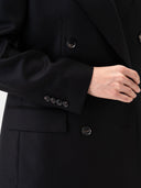 Close-up of a black blazer with buttons and a hand adjusting the sleeve. #color_black