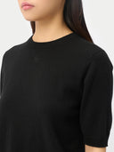 close up of a black short-sleeve, crew neck sweater top with a small dark brand logo at the top-center worn by a person on a white background #color_black