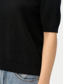 close up of a black short-sleeve sweater top worn by a person with a white background #color_black