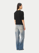 back view of a woman wearing a black sweater top and light blue jeans on a white background #color_black