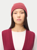 Person wearing a pink knit beanie and vest on a white background #color_madder-brown