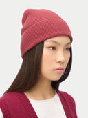 Person wearing a maroon knit beanie and cardigan on a plain background #color_madder-brown