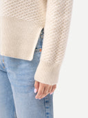 Close-up of a person wearing a beige knitted sweater and light blue jeans. #color_off-white