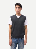 Man wearing a dark gray v-neck vest over a white shirt with blue jeans on a light gray background. #color_charcoal