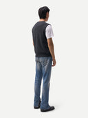 back view of a man wearing a dark gray vest over a white shirt and blue jeans on a white background. #color_charcoal