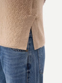 close up of a beige textured cable knit sweater with hem slit and blue jeans on a white background #color_beige