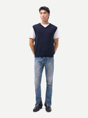 Man wearing a navy sweater vest over a white shirt with light blue jeans on a white background. #color_navy-blazer