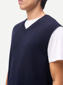 Person wearing a navy blue sweater vest over a white shirt on a plain background. #color_navy-blazer
