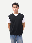 Man wearing a black sleeveless shirt over a white t-shirt with blue jeans on a plain background #color_black
