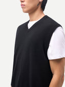 close up of a person wearing a black sweater vest over a white shirt on a light gray background #color_black