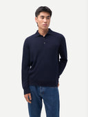 Man wearing a navy sweater polo with blue jeans on a light gray background. #color-navy
