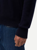 Person wearing a dark blue sweater and jeans on a white background. #color-navy