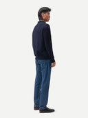 back view of a man wearing a navy sweater and blue jeans standing against a white background. #color-navy