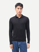 A man wearing a black long-sleeve polo knit sweater and blue jeans, standing against a light gray studio background.
