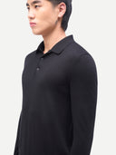 A man wearing a black long-sleeve polo shirt, shown in a side profile against a light gray studio background.