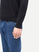 Person wearing a black sweater and blue jeans on a white background.