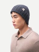 side view of a man wearing a dark gray beanie with a small brand logo and a brown polo sweater on a light gray background #color_charcoal