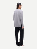 A woman shown from the back wearing a light gray knit sweater and black wide-leg trousers against a plain light gray studio background.