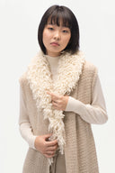 A model wearing a cream-colored, chunky knit sleeveless vest over a cream turtleneck, accessorized with a thick, shaggy cream faux-fur collar, set against a plain white studio background.