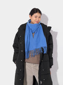 A person wearing a black puffer jacket and a blue fringed scarf. #color_blue