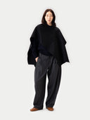Person wearing a black poncho and dark pants on a white background #color_black