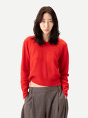 close up of person wearing a red v-neck sweater and gray pants on a white background #color_fiery-red