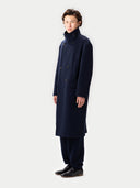 side view of man standing a long turtleneck navy coat in a white background #color_navy-blazer