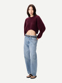 Woman wearing a oval cropped burgundy sweater and light blue jeans on a white background #color_burgundy