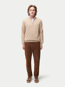 Person wearing a beige sweater and brown pants on a white background