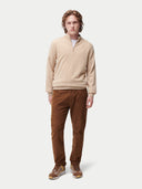 Man wearing a beige sweater and brown pants on a white background